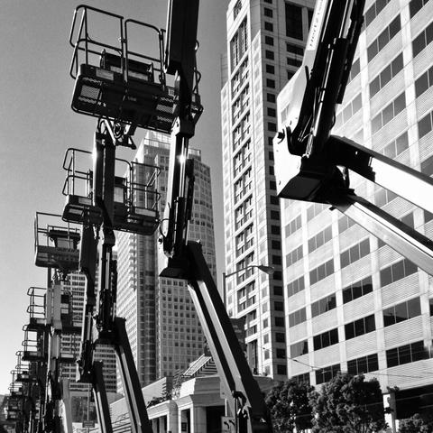 Several cherry picker type cranes with their arms raised up high in a row down a San Francisco street