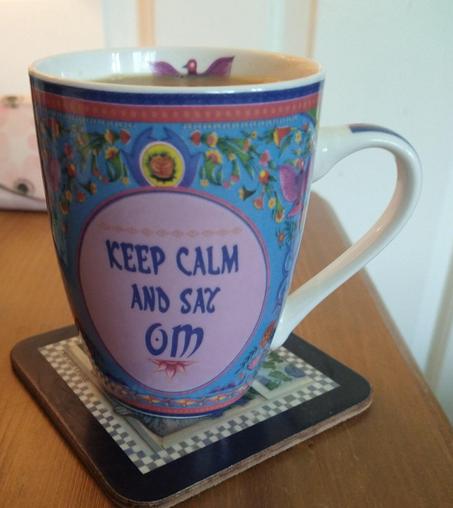 Blue floral pattern mug of tea on a bedside cabinet with a pink circle in the middle that says 
 'keep calm and say OM'