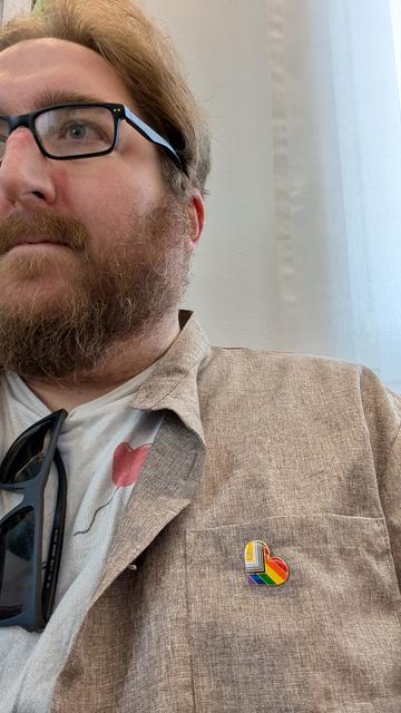 Picture of myself with the progress pride pin sitting in a waiting room