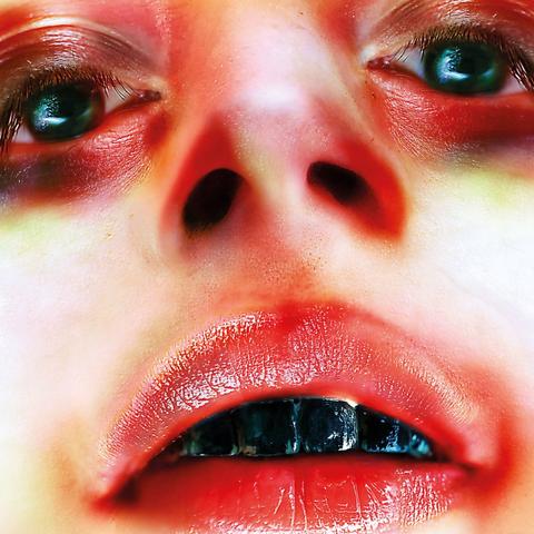 The cover art is a close-up photo of a person's face, presumably the artist's, looking into the camera. The colouring looks messed up, or perhaps it's make up, with red shadows all around the mouth, nose, and eyes. Their lips are parted, showing teeth painted black. There are no words on the cover.