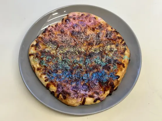 A generic margarita pizza topped with glitter in the colours of the rainbow