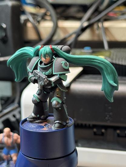 A Hatsune Miku space marine on a painting handle from Warhammer 40k. She looks into the camera.