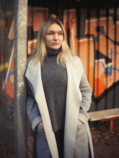 Woman standing at a bus stop that is sprayed with graffiti