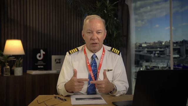 youtuber captain steeeve, an older guy in a pilots uniform at a desk, hitting a pose that looks like the bottom pleading pose of pointing index finger tips to each other
