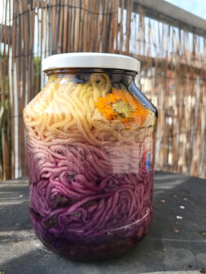 À large mason jar full of yarn. The upper third is yellow, you can also see a yellow flower pressed to the glass. The upper two thirds are a variation of pink and purple tones. There is a lot more colour on the yarn than one week before.