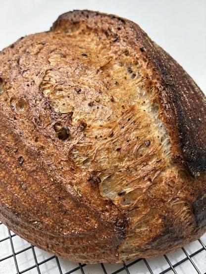 Golden coloured sourdough displaying gluten strands, seeds and herbs.