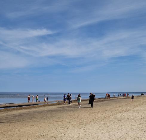 langer Strandstrand mit Spaziergehenden und Herumstehenden.