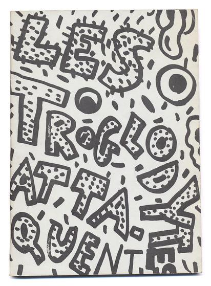 couverture imprimée en noir sur blanc.
Les mots "LES TROGLODYTES ATTAQUENT" sont écrits, de biais (comme si les mots s'écroulaient) à la main sur l'ensemble de la surface de la couverture. Le trait est épais, probablement au marqueur. Les lettres sont agrémentées de points et de traits, comme des poils ou des boutons. Il y a aussi des formes organiques qui flottent autour (des yeux schématiques et autres tubes).