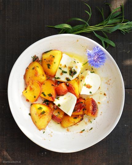 Dunkler Holzuntergrund. Weißer, eunder Teller. Darin: In Butter geschmorte, leicht karamellisierte Nektarine mit Zwiebelgranulat, Estragon und Mozzarella