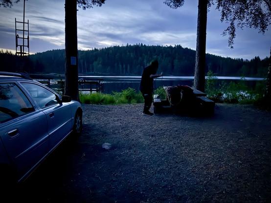 Man står vid picknickbord och ordnar med fiskespöt. Bakom en sjö. Nattetid.
