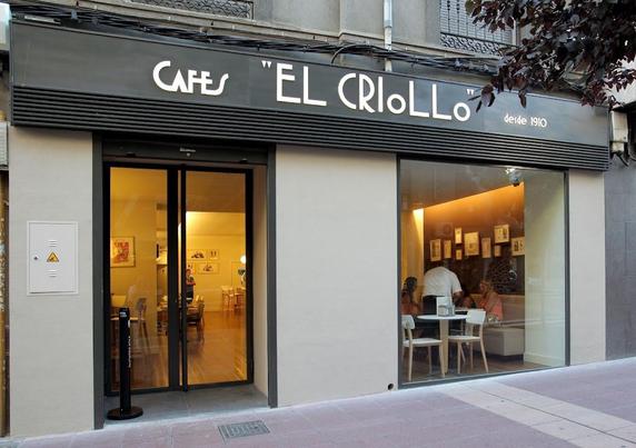 The exterior of a cafe called "Cafes 'EL CRIOLLO' desde 1910" with people inside.