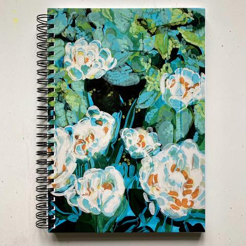 An overhead shot of a spiral notebook on an off-white table cloth. The notebook cover is a partial image of the abstracted white tulip painting.