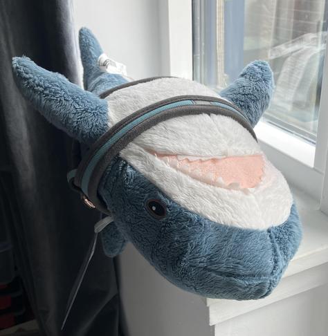 A Blåhaj cuddly shark lying on its back on a windowsill.