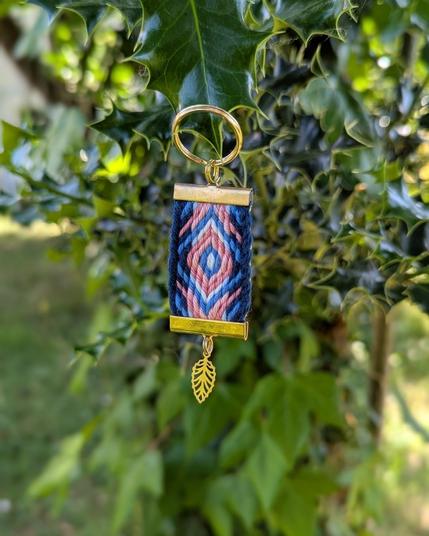 Photo d'un porte-clés tissé aux couleurs du drapeau trans posé sur une brache de houx.
