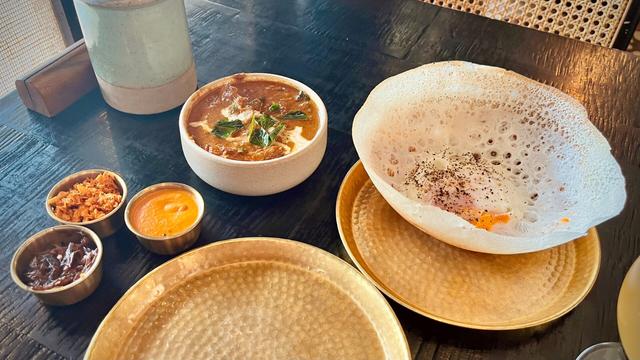 Egg hopper, Lankan chicken kari, tomato chutney, pol sambol, and seeni sambol at Hoppers Kings Cross. 
Differently sized bowls with food on a table.
