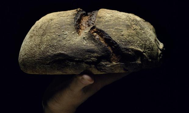 Hombre sosteniendo una hogaza de pan, primer plano, vista lateral (Getty Images)