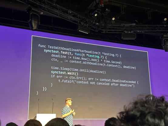 A person stands in front of a conference slide with go code demonstrating the new synctest package.