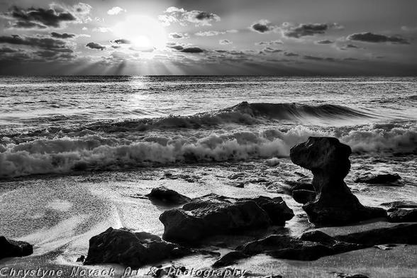 Where Stone Gazes At The Sky is a black and white photograph capturing the serene beauty of the morning sun rising over the ocean with beams of light breaking through the clouds and the spectacular rock formations along Coral Cove Park's shoreline located in Florida.