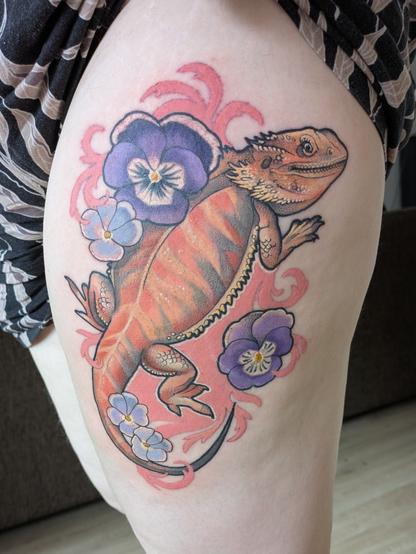 Fresh tattoo on my upper thigh of an orange bearded dragon surrounded by dark and light purple pansies and a pink swirly background.