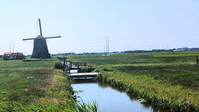 A windmill in a field a ditch in the middle.