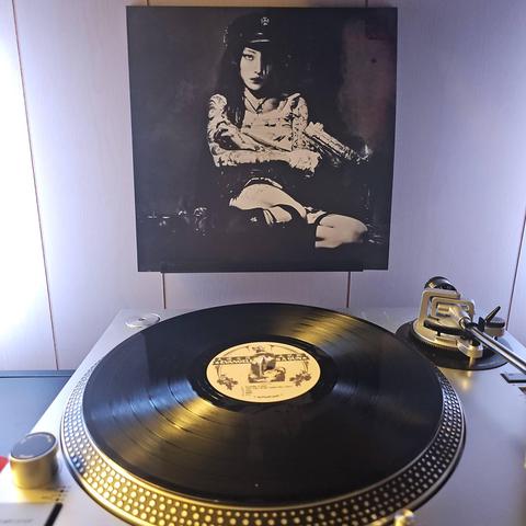 A vinyl record sits on a turntable. Behind the turntable, a vinyl album outer sleeve is displayed. The front cover shows yeule holding a gun while sitting in a corner.