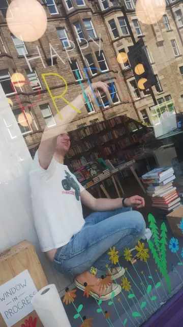 Bookseller Jack painting the Happy Pride sign in the window of the Edinburgh Bookshop