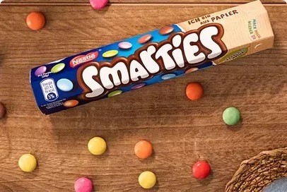 Eine Packung Smarties von Nestlé auf einem Holztisch mit einigen bunten Smarties drum herum.