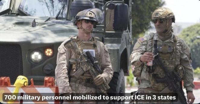 Two military personnel stand near a military vehicle, both wearing tactical gear and holding weapons. One soldier is looking at the camera while the other appears to be sipping from a beverage. Background includes trees and a barricade with construction cones. “700 MIL personnel mobilized…”: