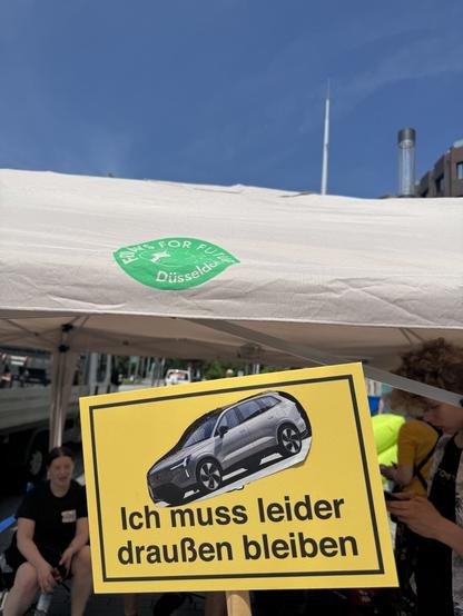 Ein gelbes Schild zeigt ein Auto. Darunter steht „Ich muss leider draußen bleiben“.