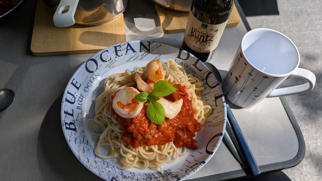 Eine Portion Spaghetti Putanesca mit Scampi und einer Tasse Wein (kein Glas vorhanden)