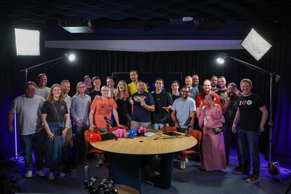 PHPverse hosts, speakers and live audience all standing next to each other posing for a photo in the studio behind the table at which the online conference was recorded.