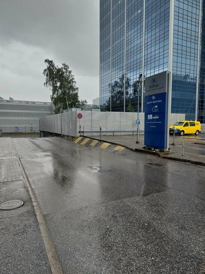 A high office building next to a parking lot. A yellow airport staff van is parked next to the building