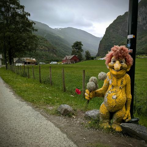 A photograph of a yellow troll statue standing in front of a telegraph pole in a Norwegian valley.