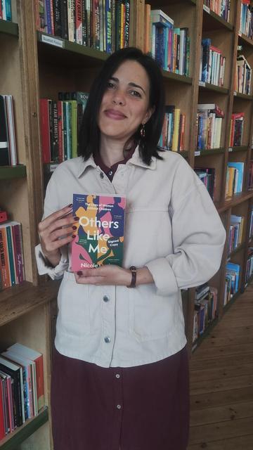 Author Nicole Louie holding the paperback of her new book, Others Like Me, in the Edinburgh Bookshop