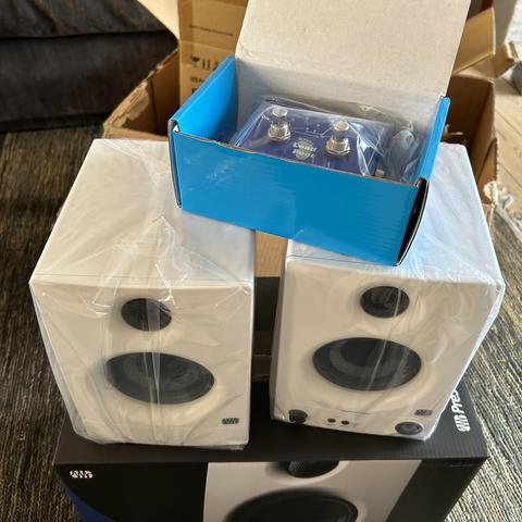 a pair of white Eris 3.5 active speakers on top of their box, still in plastic, and on top of them a Leadfoot ABY switcher pedal inside its blue cardboard box