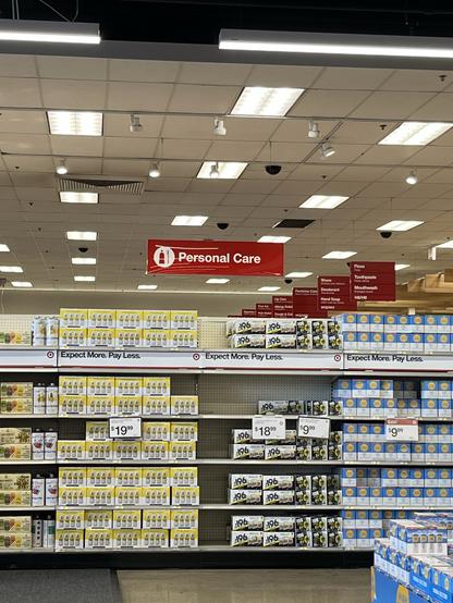 An interior view of a retail store aisle labeled "Personal Care". Shelves display various cases of alcohol, with price tags visible. The signage highlights discount promotions.