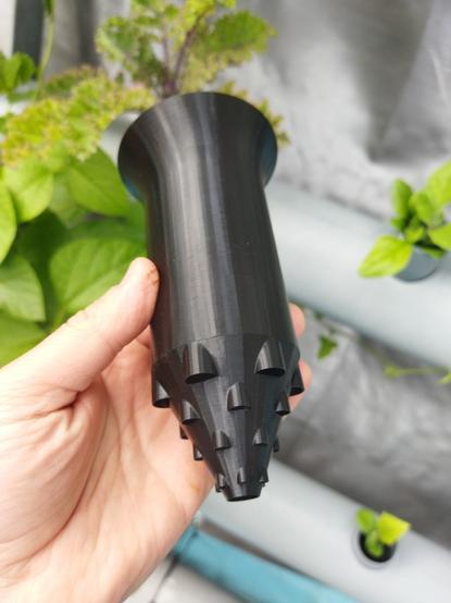 3d printed tall net cup with solid upper parts and open cylindrical holes on a conical part at the bottom, the way you do open holes in a vase mode 3d print. Vertical garden in the background