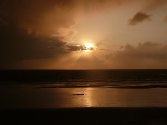 Abendsonne über dem Meer hinter einer Wolke verborgen
Im Vordergrund Strandbereiche bei Ebbe