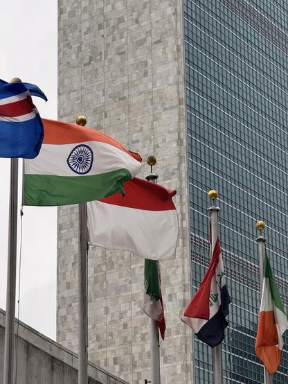 Flags of several countries, including India, Indonesia, and Iraq, are displayed in front of the United Nations HQ.
