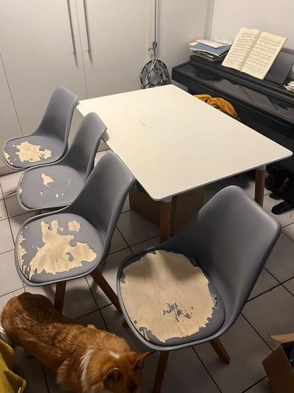photo d’une table rectangulaire blanche avec des pieds en bois clair + des chaises grises dont les assises sont abîmées