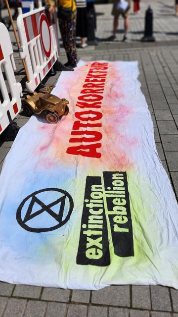 Zu sehen ist ein weißes Banner mit der Aufschrift AUTOKORREKTUR und das Extinction Rebellion Logo.