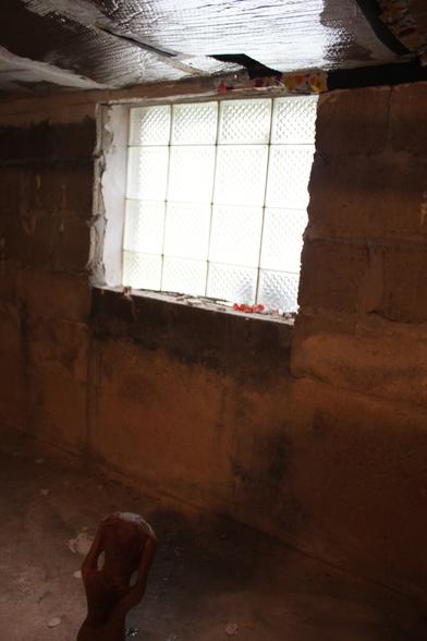 Glow from a square window, dirty walls and floor, metallic insulation on ceiling. Unidentifiable figurine close to bottom