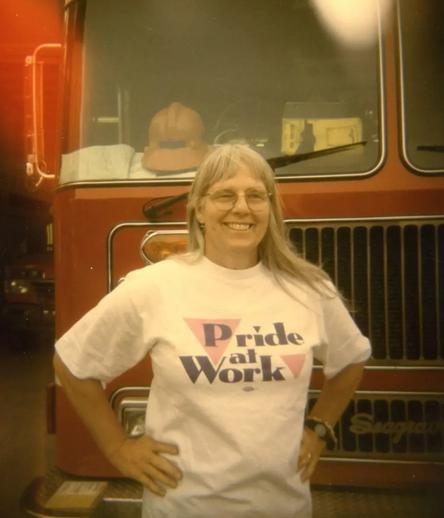 In this picture provided by her widow Janis Walworth, Michele Kaemmerer smiles while standing in front of a fire truck. She is wearing a white t-shirt with pink triangles that reads "Pride at Work."