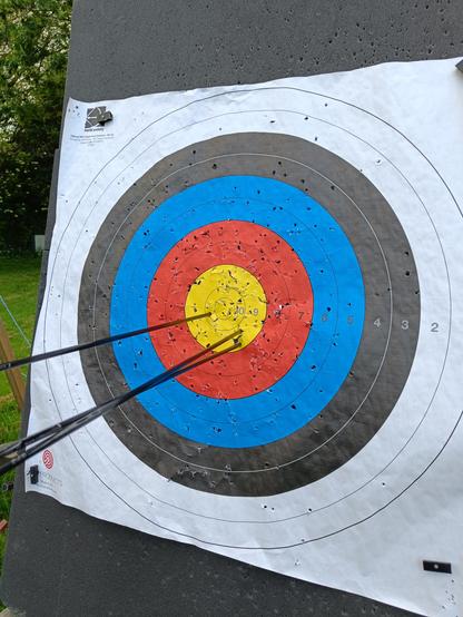An archery target with three arrows, all in the yellow. Two 9s to the bottom right of center, and one 10 to the left of center.
