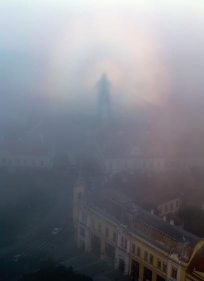 2014 August 23

The Spectre of Veszprem
 * Image Credit & Copyright: Tamas Ladanyi (TWAN)

Explanation: 
The city of Veszprem, Hungary was only briefly haunted by this mysterious spectre. On the morning of August 11, its monstrous form hovered in the mist above municipal buildings near the town center. A clue to its true identity is offered by the photographer, though, who reports he took the picture from the top of a twenty story building with the rising Sun directly at his back. That special geometry suggests this is an example of an atmospheric phenomenon called the Glory or sometimes "the Spectre of the Brocken". Also seen from mountain tops and airplanes when looking opposite the Sun, the dramatic apparition is the observer's shadow on clouds or fog, the small droplets of water scattering light back towards the Sun through complex internal reflections. Careful night sky watchers can also encounter this spectre's analog in astronomy, a brightening of zodiacal light opposite the Sun known as the gegenschein. 

Authors & editors: Robert Nemiroff (MTU) & Jerry Bonnell (UMCP)
NASA Official: Phillip Newman Specific rights apply.
NASA Web Privacy Policy and Important Notices
A service of: ASD at NASA / GSFC
& Michigan Tech. U.