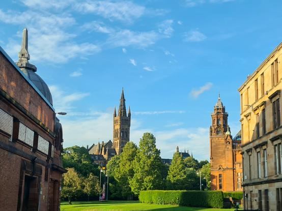 A view down a street lined with tenements to the gothic tower of Glasgow University rising above the trees of Kelvingrove Park.