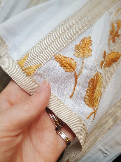 A lovely little sprig in the same orange hued thread, with two leaves on it. Done in stem stitch, and with staggered blanket stitch for the leaves, it's simple but pretty effective. Next to it, on the right, is more of the same. It's sewn on top of a flat felled seam, with a boning channel and the petersham binding on the edge next to it. Not a great work of art, but it's there.