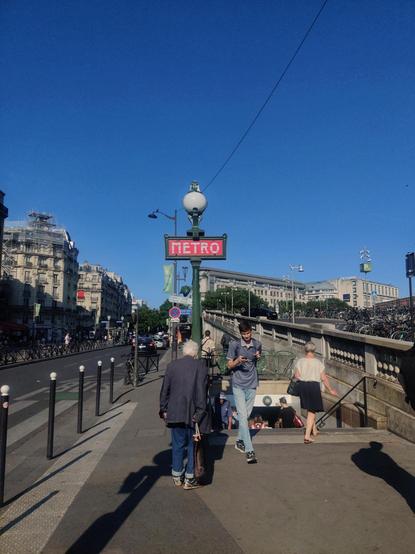 Entrada a la estación de metro Gare de Lyon. Hay gente que sale y entra. A la izquierda hay una señal verde con un cartel rojo que dice "metro"
