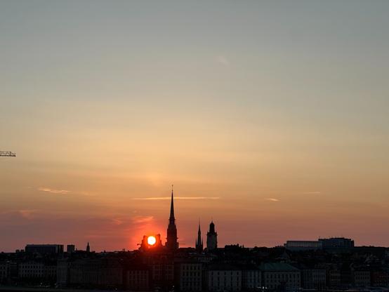 The setting sun nestled neatly in the middle of the silhouette of a pair of buildings on the horizon, to where it looks like a wrench or mechanical hand gripping it