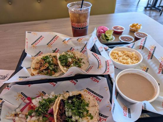 A tray showing four tacos, rice, beans, salsa and iced tea.